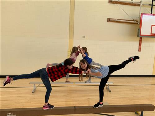 2 students hold hands on a balance beam with their back legs extended 